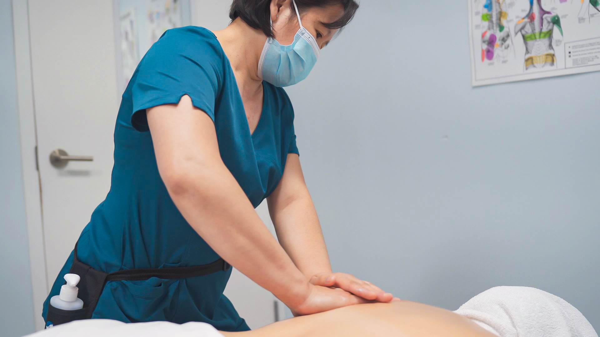 Massage therapist in a mask treating a patient's back