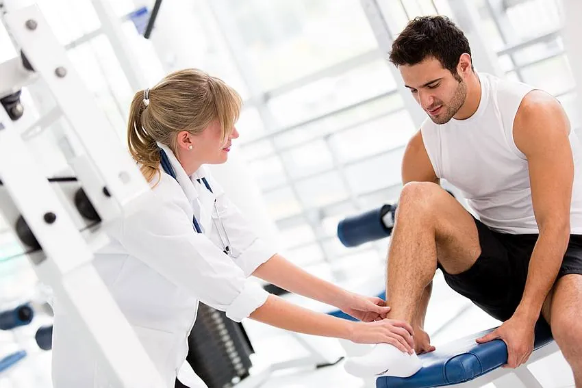 Physiotherapist assessing an athlete's ankle injury in a gym